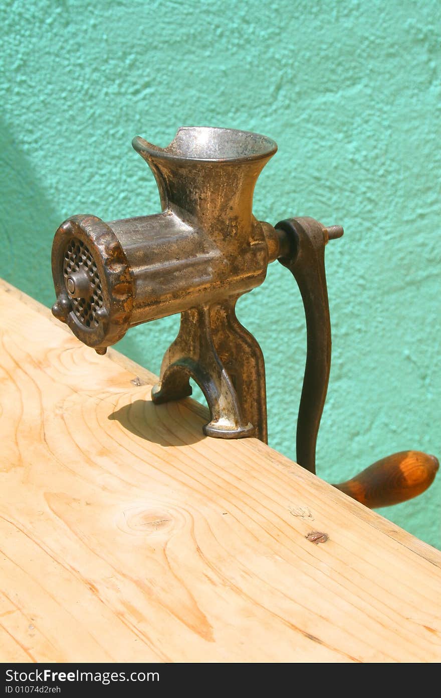 Antique meat grinder on weathered wooden table against turquoise wall