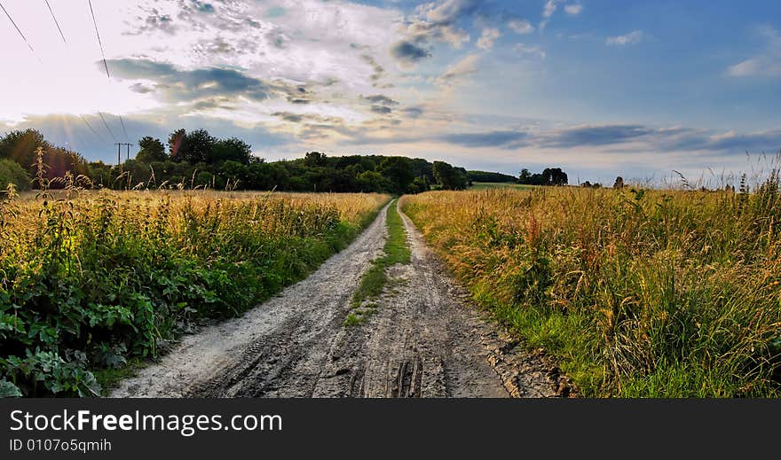 Field earth road in time sunset with cloudy sky. Field earth road in time sunset with cloudy sky