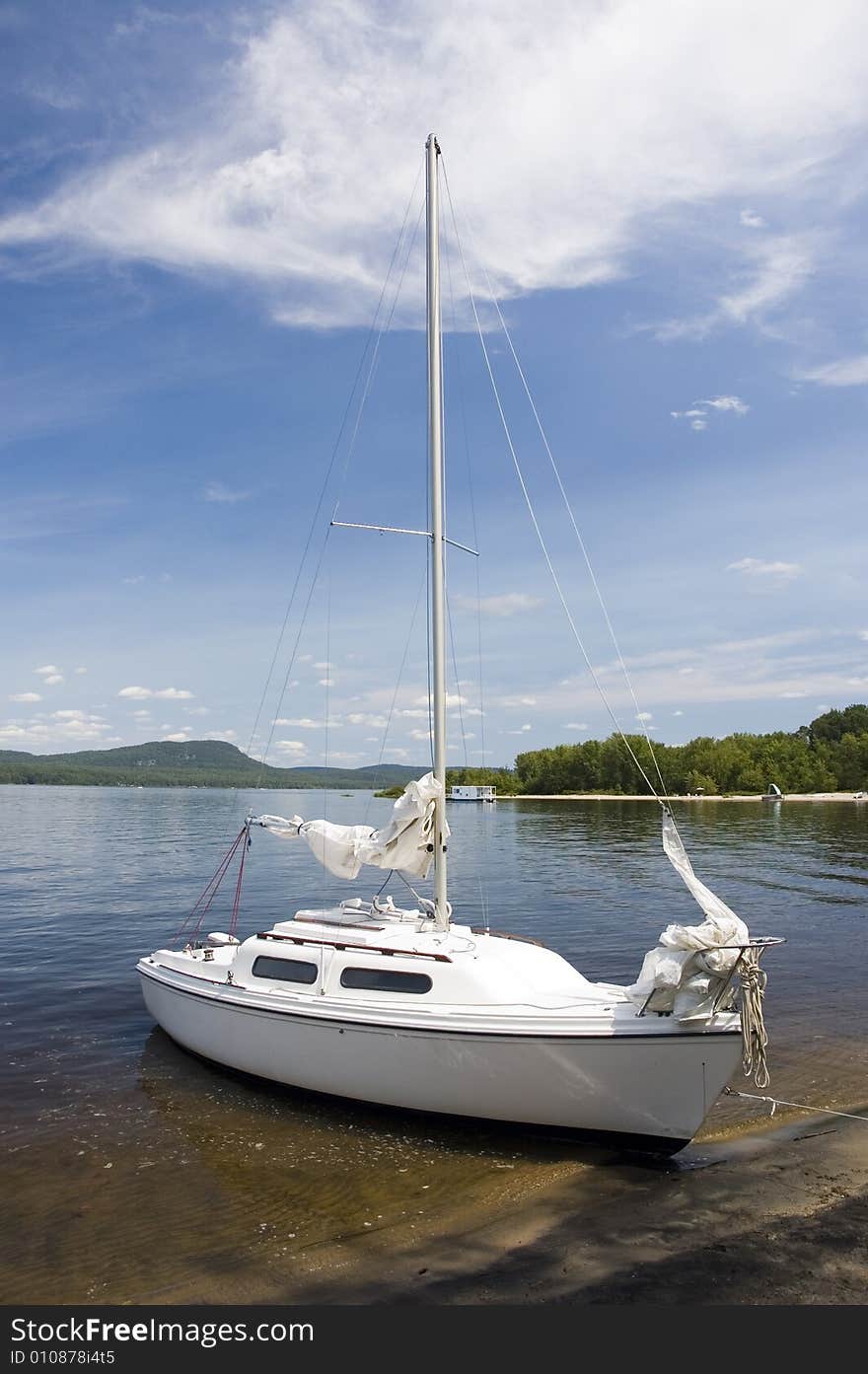 A small white sail boat near the shore