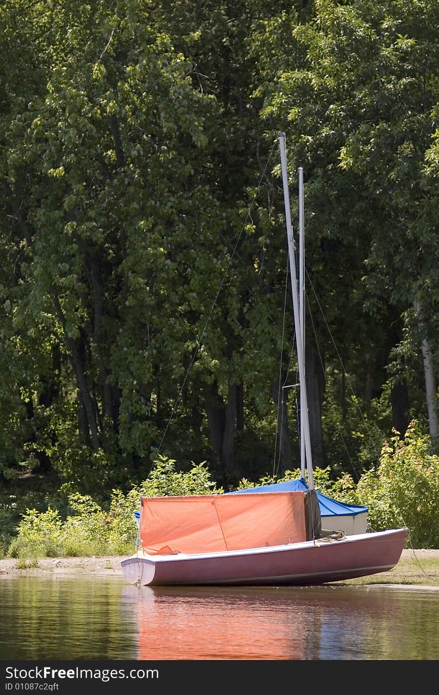 A small orange sail boat near the shore