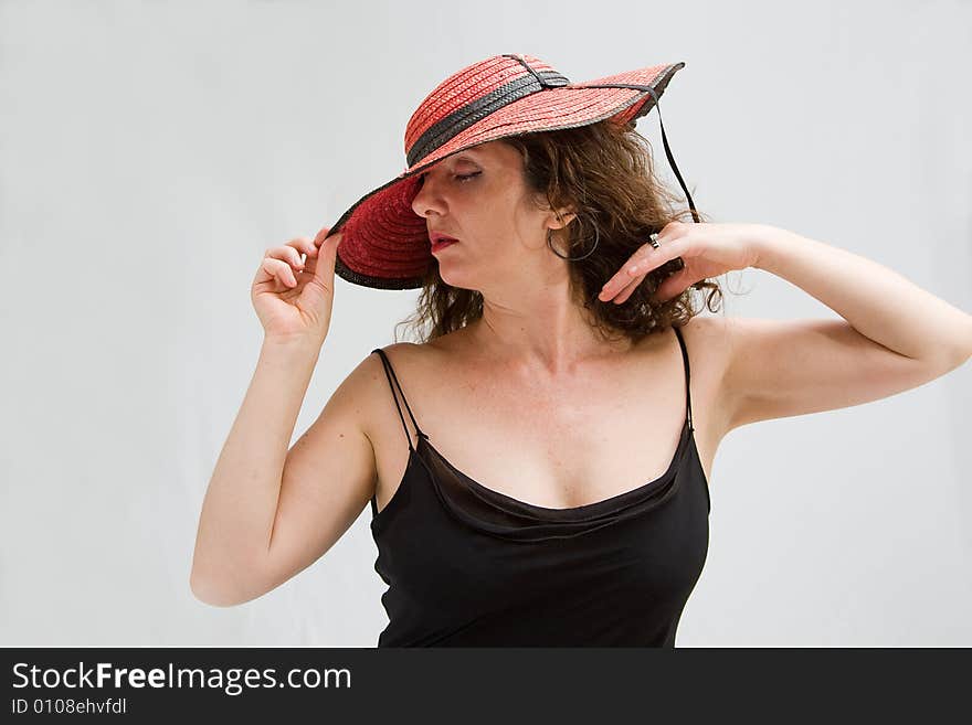 Serene middle aged woman wearing a red hat tipping it over with 1 hand, isolated. Serene middle aged woman wearing a red hat tipping it over with 1 hand, isolated