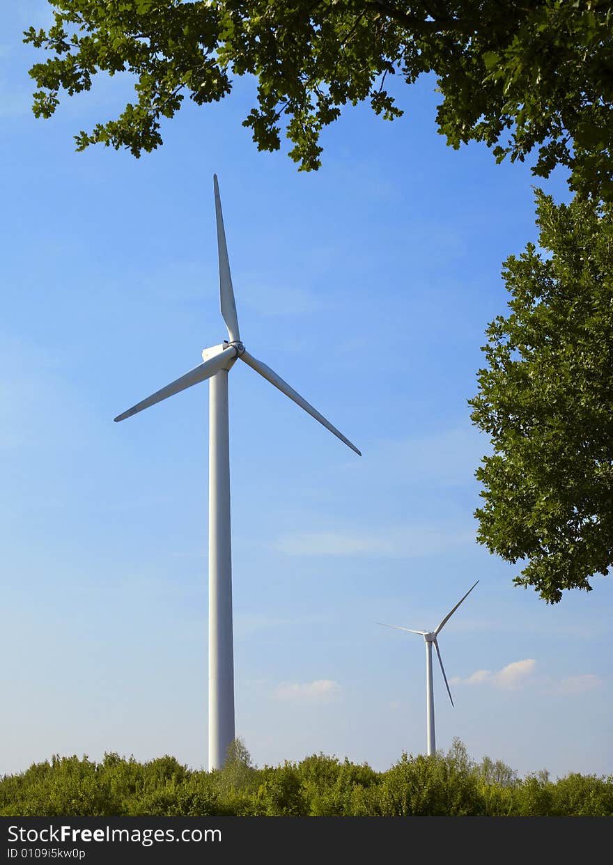 Two windmills in front of the blue sky, frame of trees. Two windmills in front of the blue sky, frame of trees