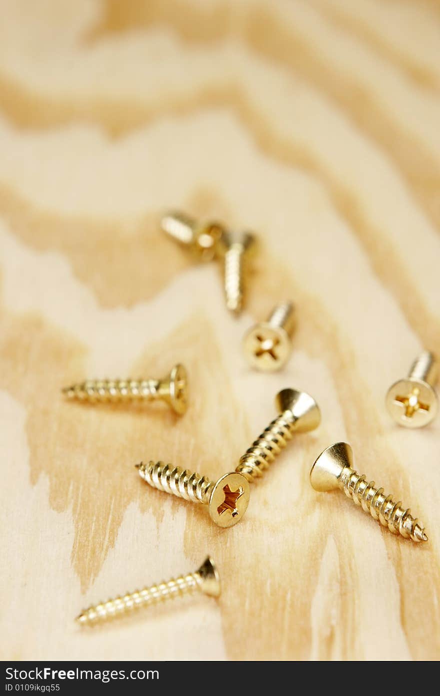 Brass screws randomly laying on plywood. Brass screws randomly laying on plywood