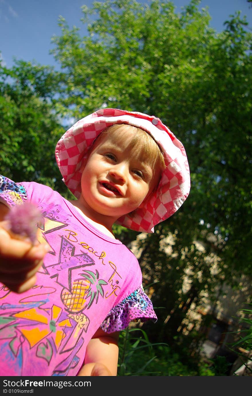 Little smiling girl with a flower against a tree