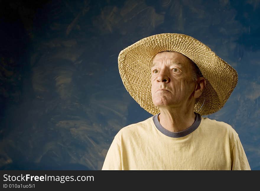 Senior man in a straw hat in front of blue set wall. Senior man in a straw hat in front of blue set wall