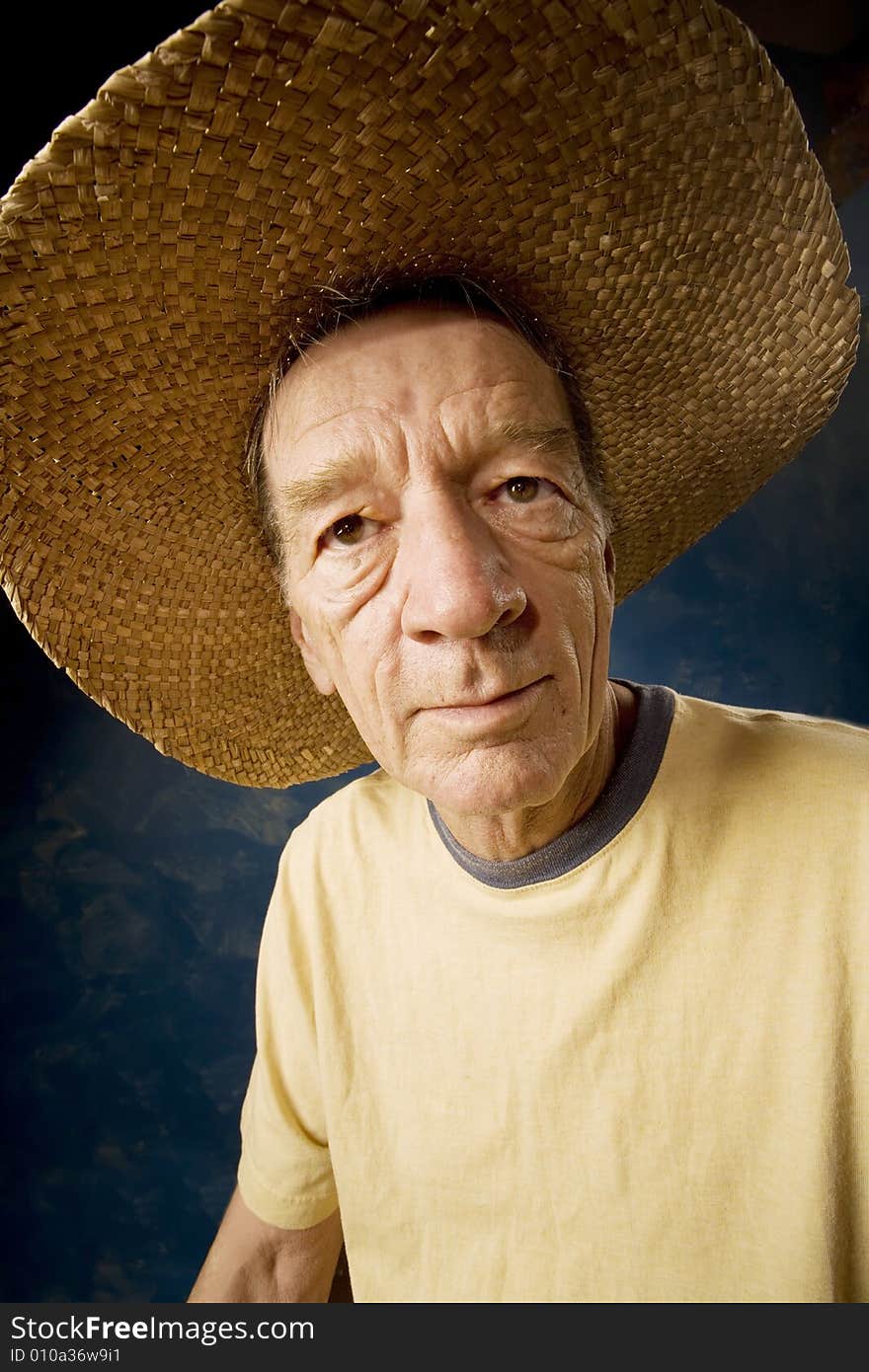 Senior man in a  big straw hat in front of blue set wall. Senior man in a  big straw hat in front of blue set wall