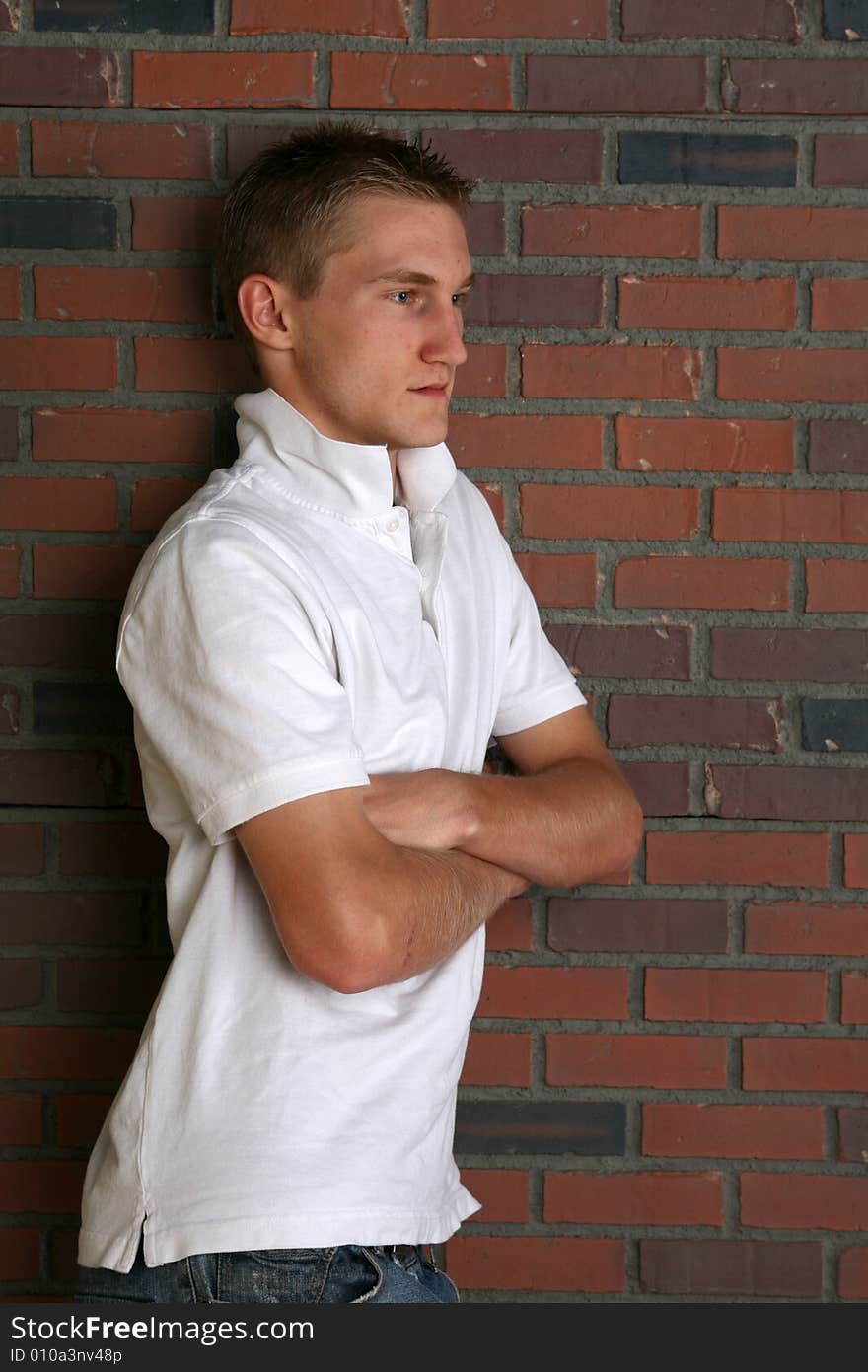 Buff and slim looking young man standing next to brick wall with arms crossed. Buff and slim looking young man standing next to brick wall with arms crossed