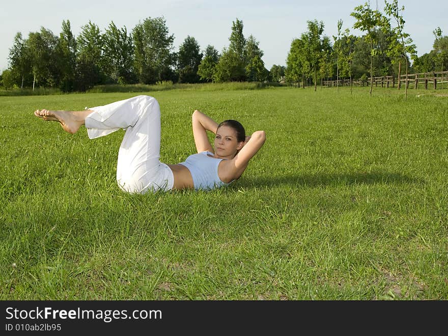 Sporty girl exercising on meadow against the sky.