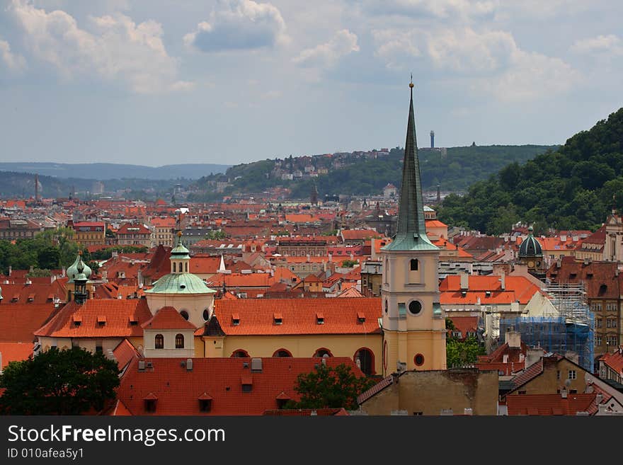 Tiled red roofs of old town, Part of green hill, and tall broach at cloudy day. Prague, Petrzin, Hrad. Tiled red roofs of old town, Part of green hill, and tall broach at cloudy day. Prague, Petrzin, Hrad.