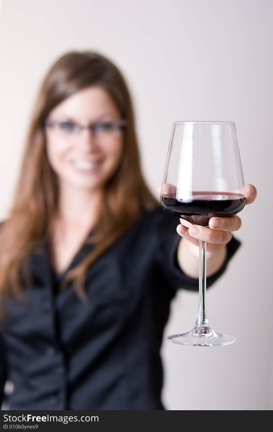 Modern young woman holding a wine glass with liquid in it doing a cheers motion. Focus in glass. Modern young woman holding a wine glass with liquid in it doing a cheers motion. Focus in glass.