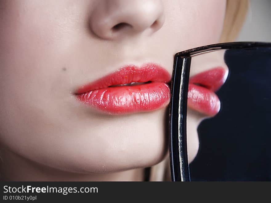 Scarlet lips are reflected in a little mirror which a girl holds in a hand