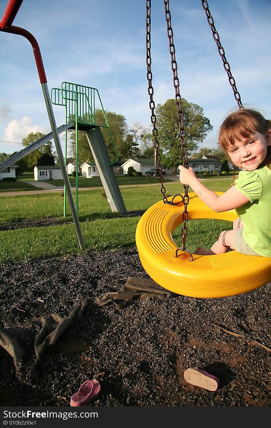 An adorable little girl swinging at the playground. An adorable little girl swinging at the playground