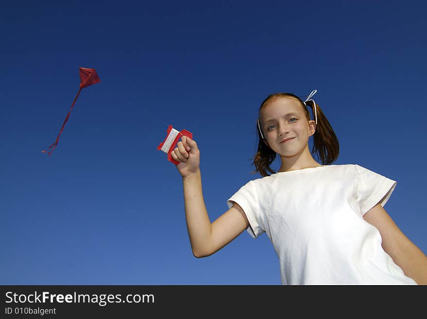 Girl wearing white shirt flying a kite with blue sky