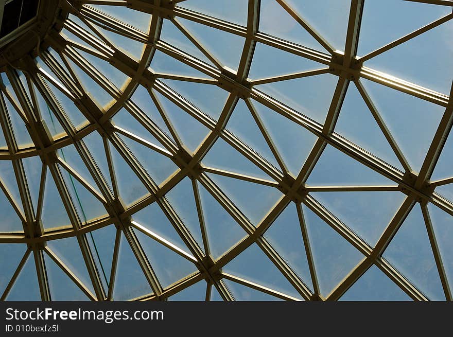 Silver metal curved roof joists in a conservatory with glass panes in between and a blue sky. Silver metal curved roof joists in a conservatory with glass panes in between and a blue sky