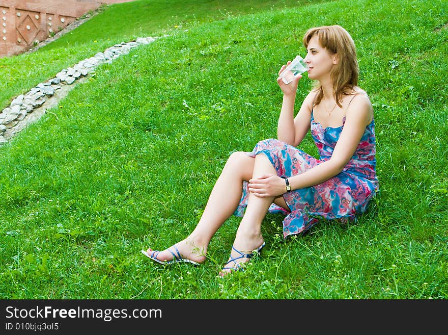 Girl drinks water from a glass sitting on a green grass. Girl drinks water from a glass sitting on a green grass