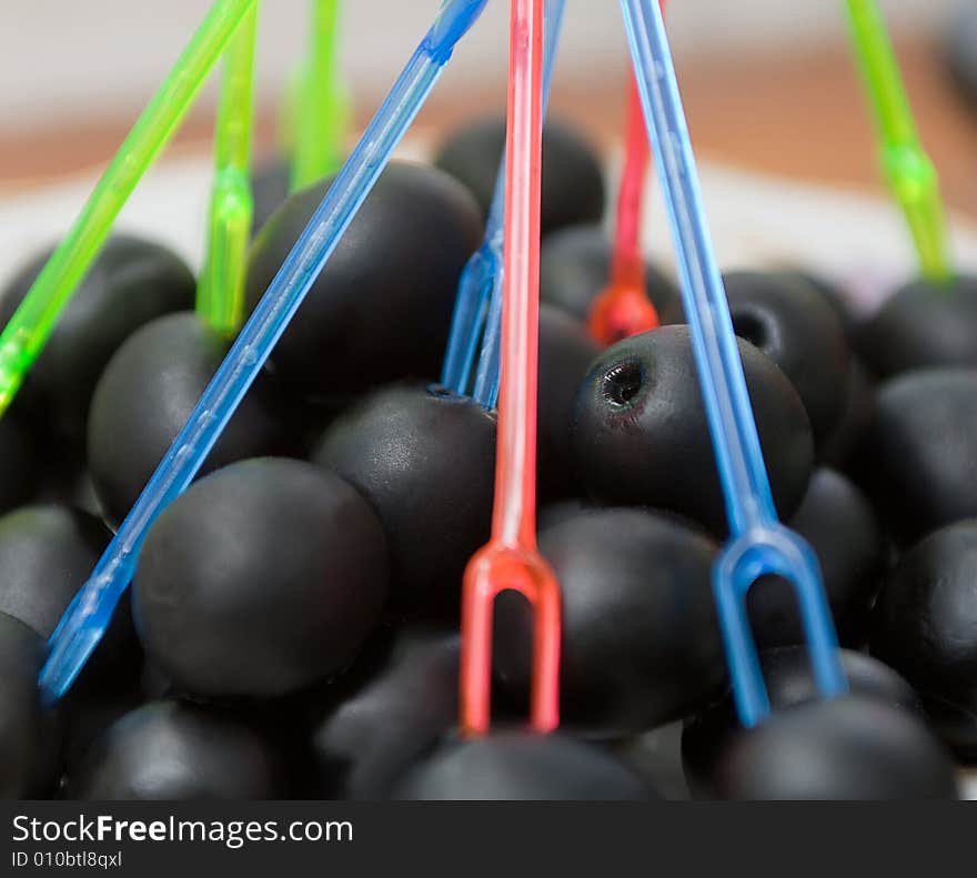 Black tinned olives lying on a plate, with colorful pick in them. Black tinned olives lying on a plate, with colorful pick in them