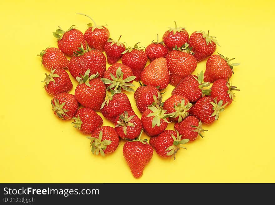 Strawberries on a yellow background in shape of a heart. Strawberries on a yellow background in shape of a heart