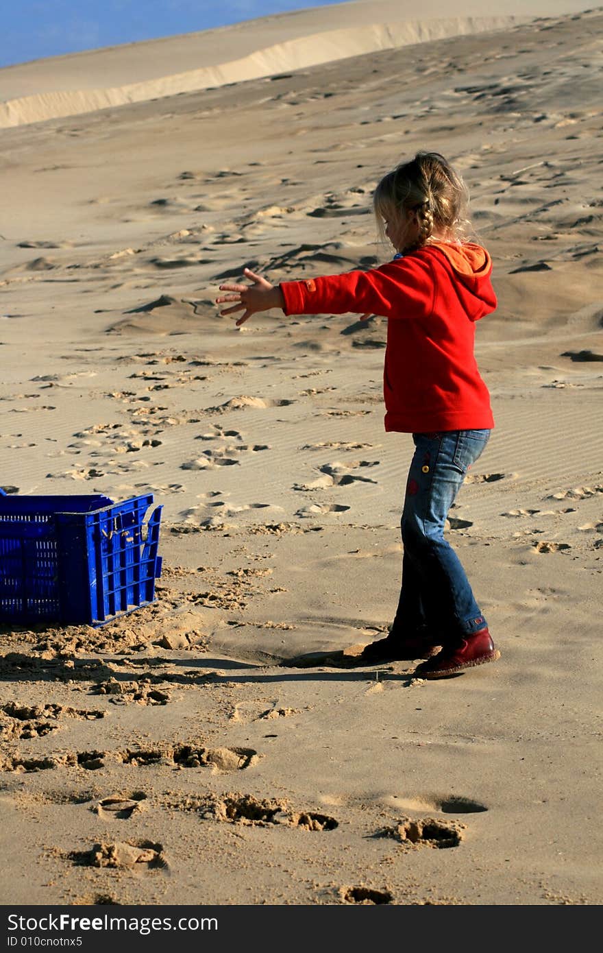 A beautiful white caucasian girl child playing with a blue container on the beach. A beautiful white caucasian girl child playing with a blue container on the beach