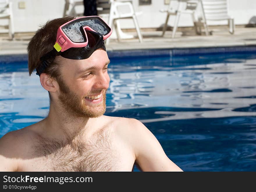 A Man is standing in a pool. He is smiling and looking away from the camera. He is wearing goggles. Horizontally framed photo. A Man is standing in a pool. He is smiling and looking away from the camera. He is wearing goggles. Horizontally framed photo.