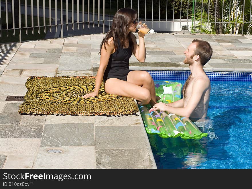 A young, attractive couple are beside the pool, staring and drinking. - horizontally framed. A young, attractive couple are beside the pool, staring and drinking. - horizontally framed