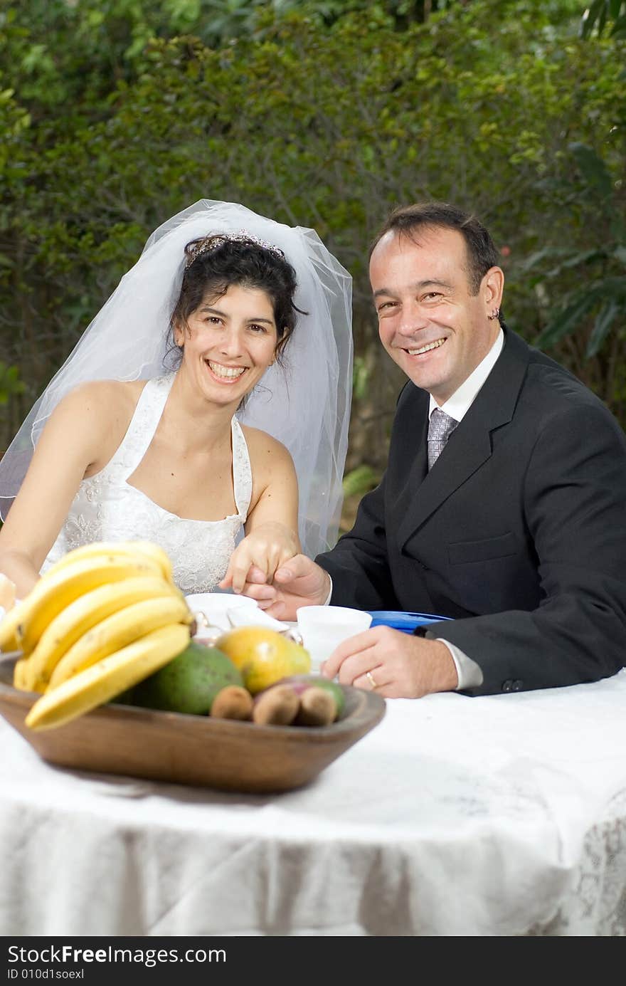 A newly married couple, at a table with fruits on it, smile for the camera together. - vertically framed. A newly married couple, at a table with fruits on it, smile for the camera together. - vertically framed