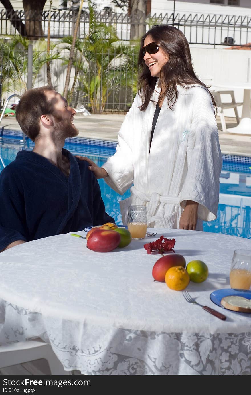 A young, attractive couple, the man sits down in a black robe, at a fruit covered table, the woman stands next to him in a white robe. - vertically framed. A young, attractive couple, the man sits down in a black robe, at a fruit covered table, the woman stands next to him in a white robe. - vertically framed