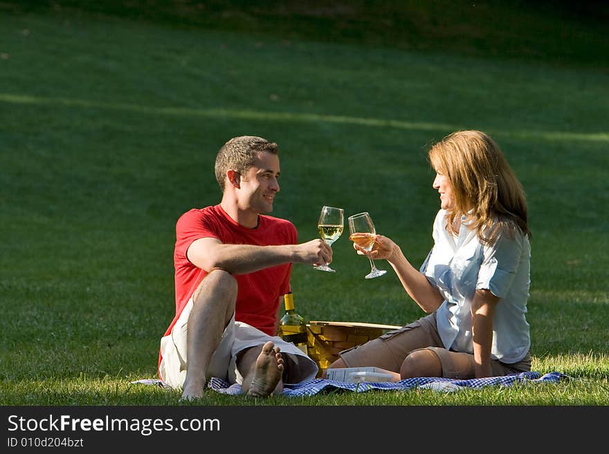 A couple, sitting down, drink together in a park. - horizontally framed. A couple, sitting down, drink together in a park. - horizontally framed