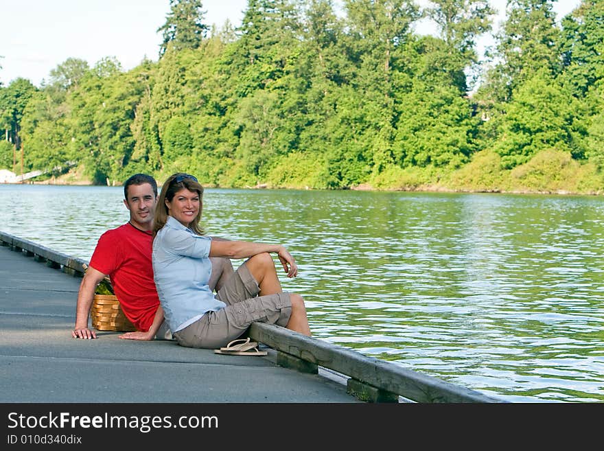 A young couple, sit on a lake dock, together. - horizontally framed. A young couple, sit on a lake dock, together. - horizontally framed