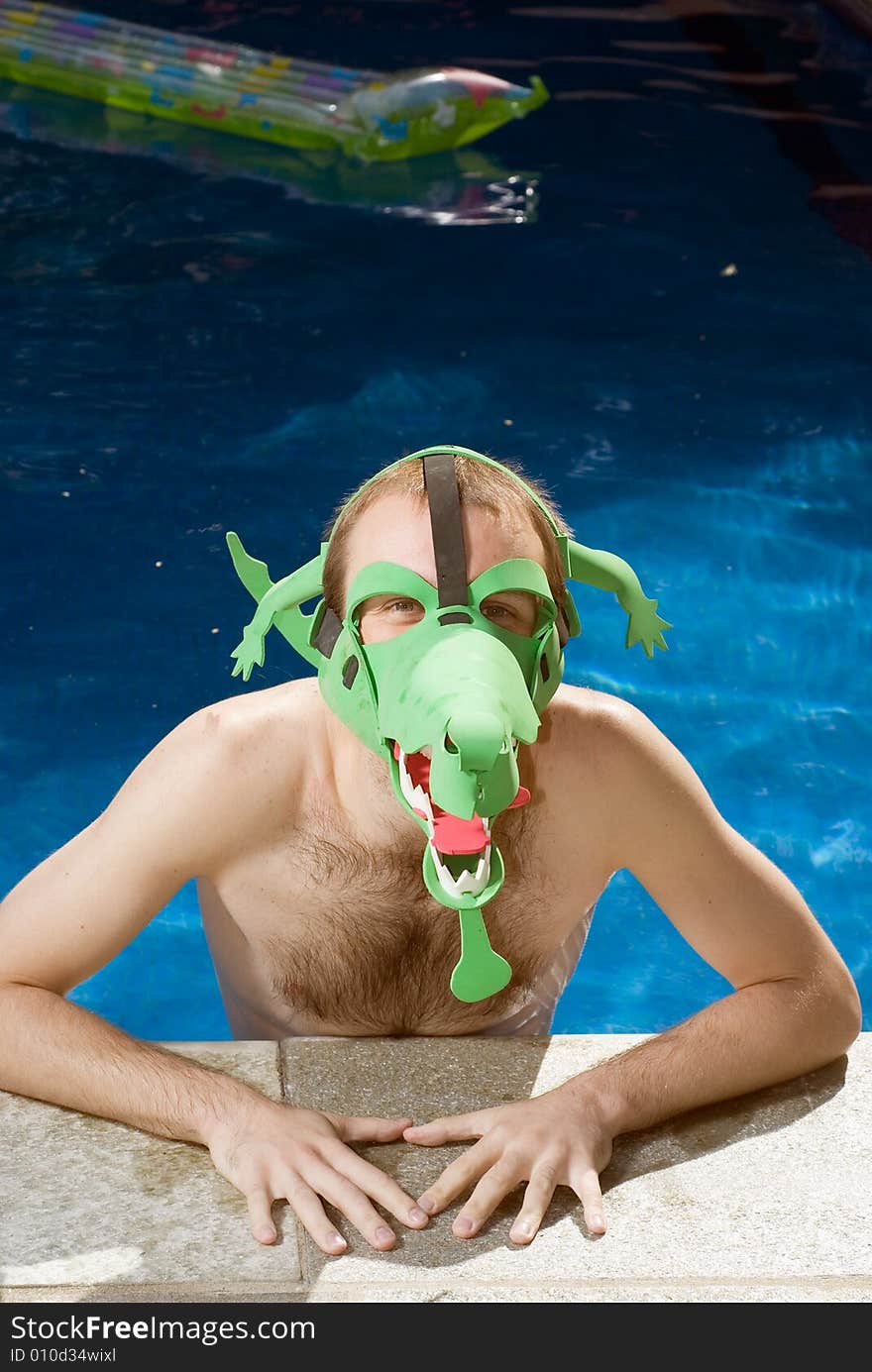 A man, in the pool, looks at the camera while wearing a funny, green crocodile mask. - vertically framed. A man, in the pool, looks at the camera while wearing a funny, green crocodile mask. - vertically framed