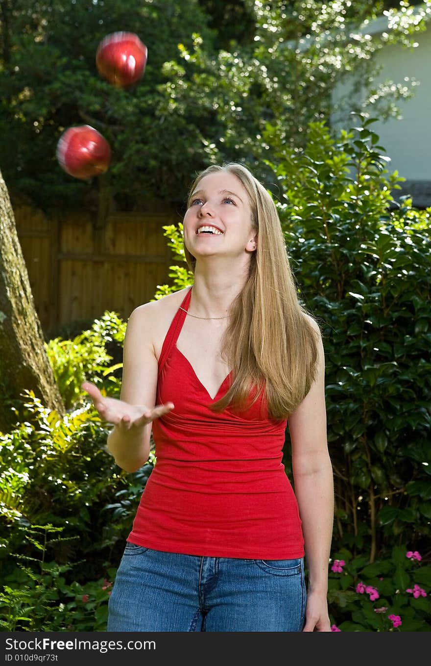 Pretty blond young woman/teenager juggling two apples outdoors. Pretty blond young woman/teenager juggling two apples outdoors