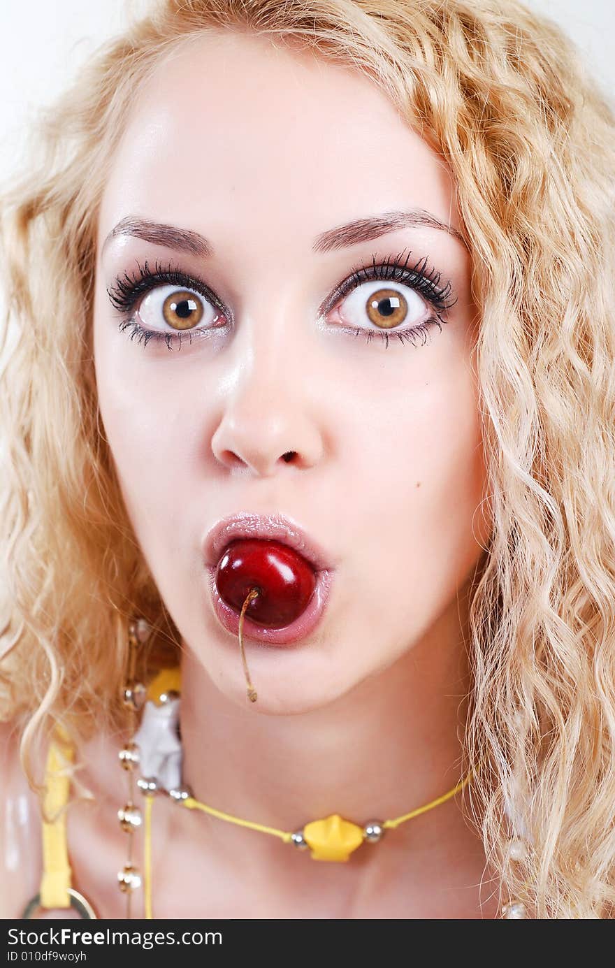 Beauty young woman with opened surprised eyes and red cherry in mouth