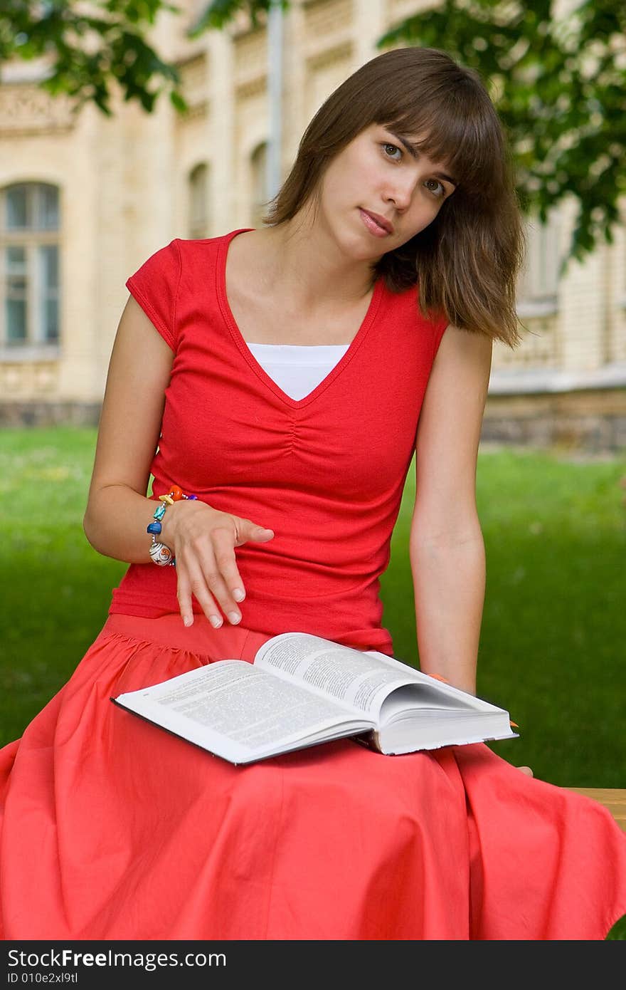 A beautiful young college girl reading a book outdoors. A beautiful young college girl reading a book outdoors