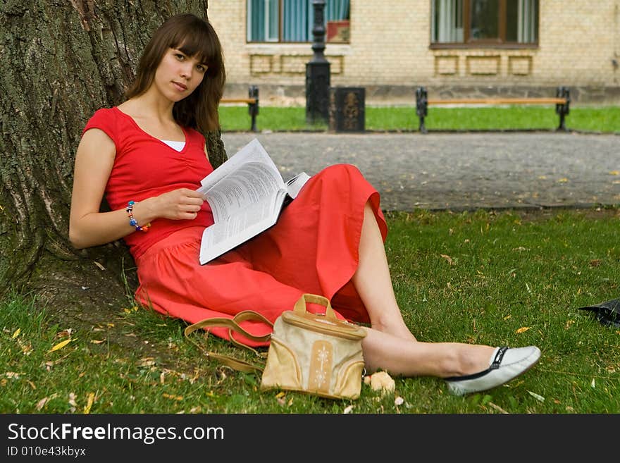 A beautiful young college girl under a tree reading a book. A beautiful young college girl under a tree reading a book