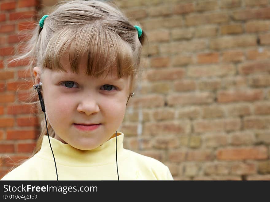 The young nice girl listens to music on a background of a brick wall