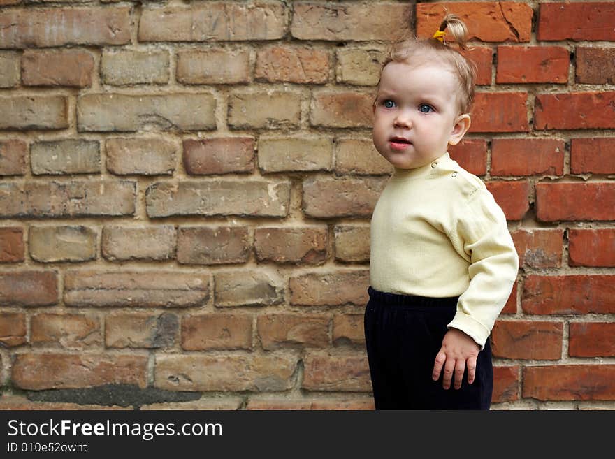 An image of baby-girl near a yellow brick wall