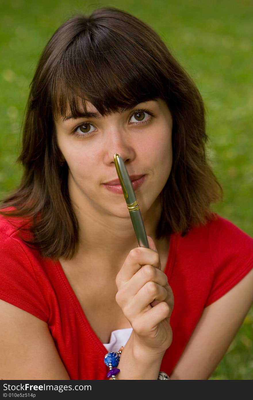 A beautiful young college girl holding a pen near her nose. A beautiful young college girl holding a pen near her nose