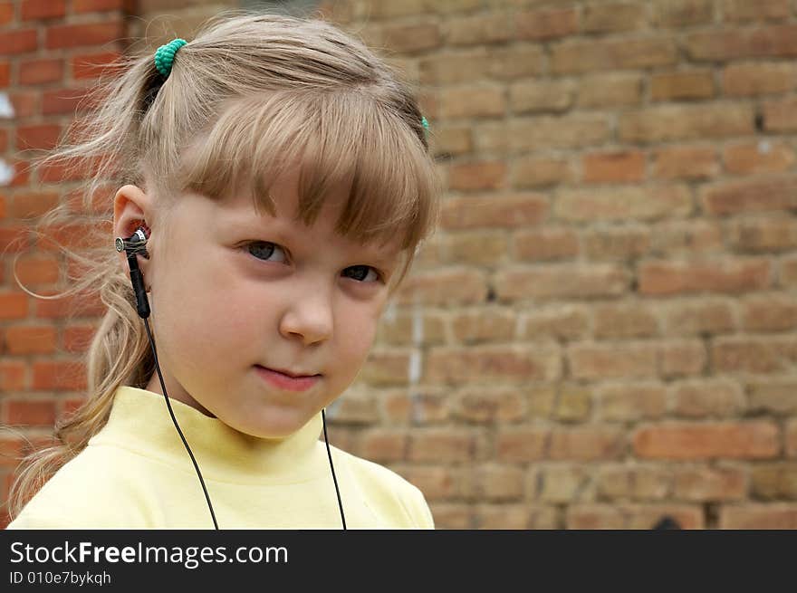 The young girl listens to music on a background of a brick wall. The young girl listens to music on a background of a brick wall