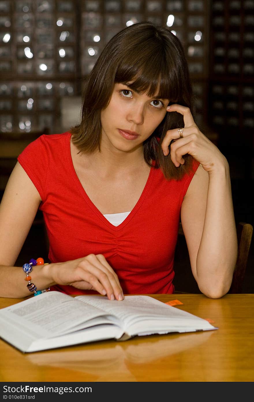 A beautiful young college girl reading a book in a library. A beautiful young college girl reading a book in a library