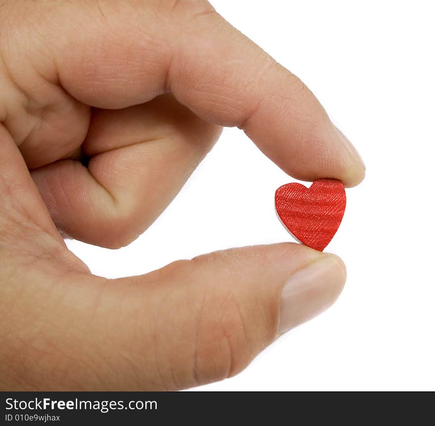 A hand shows a small wood and painted red heart between it's two fingers in front of a white background. A hand shows a small wood and painted red heart between it's two fingers in front of a white background.