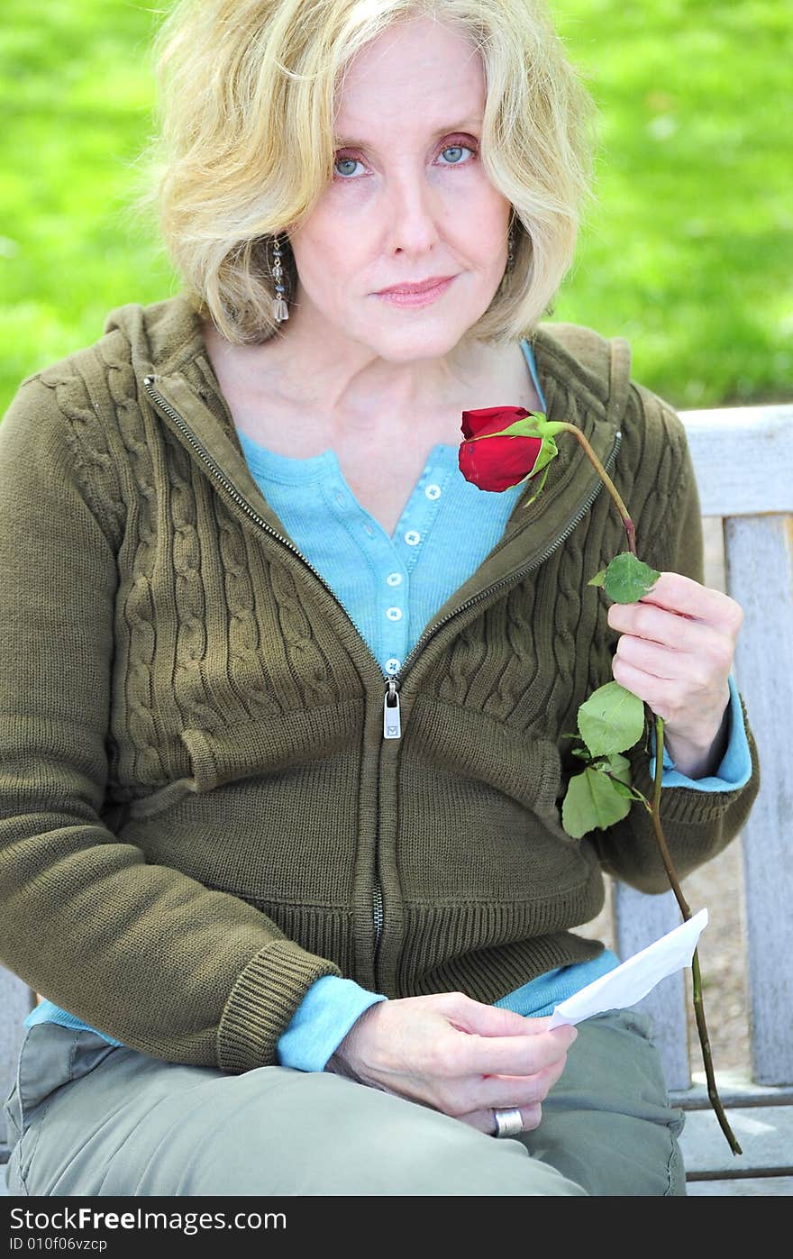 Woman smelling a rose while sitting on a park bench. Woman smelling a rose while sitting on a park bench.