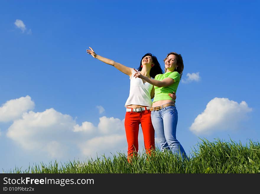 Two young women on a green meadow and show something