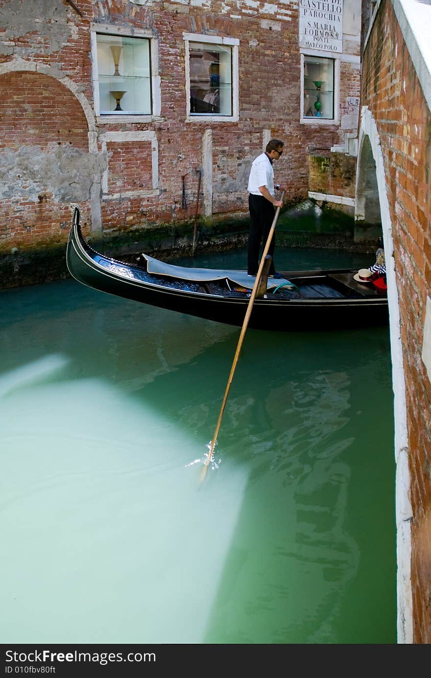 Venetian gondolier on his gondola in a waterway if Venice