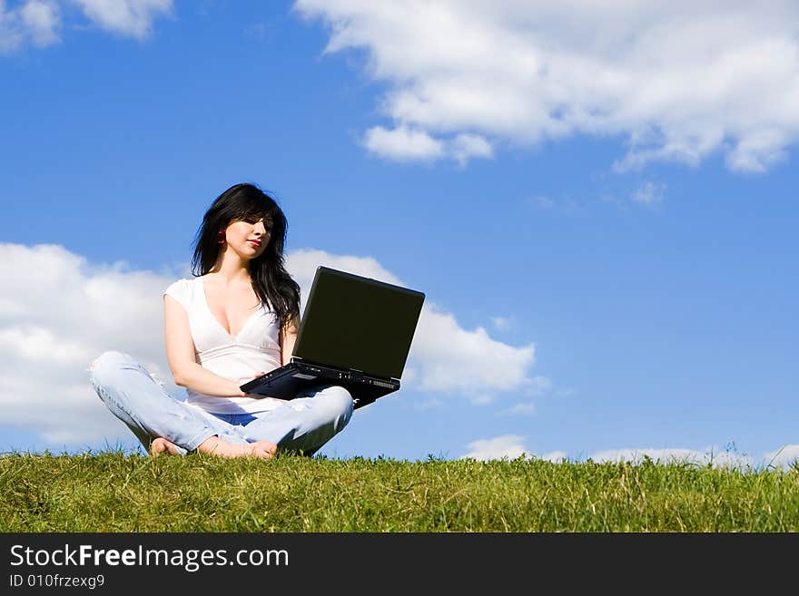 Pretty woman with laptop on the green grass