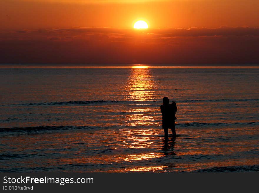 A mother and small child wade into the water during a beautiful sunset. A mother and small child wade into the water during a beautiful sunset