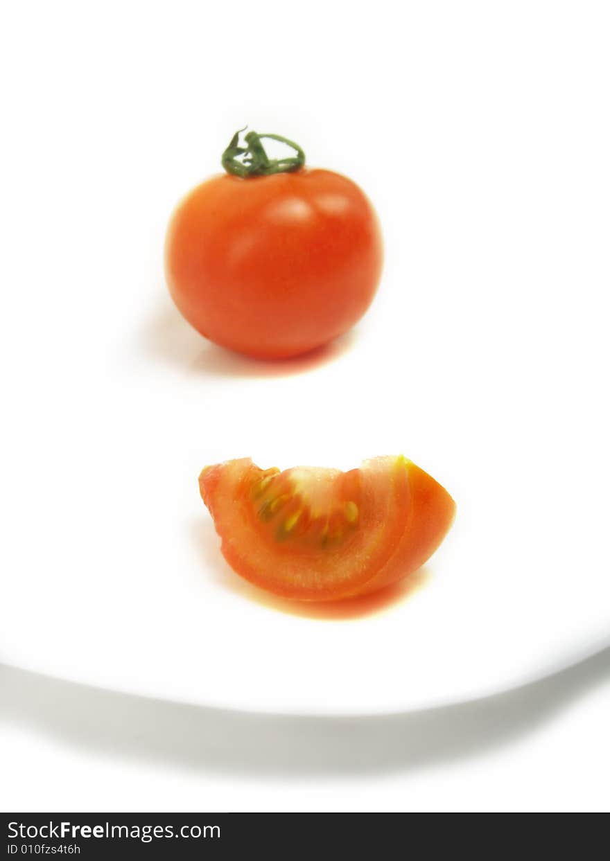 A slice of tomato and a blurred whole one on a white plate and isolated on white background. A slice of tomato and a blurred whole one on a white plate and isolated on white background