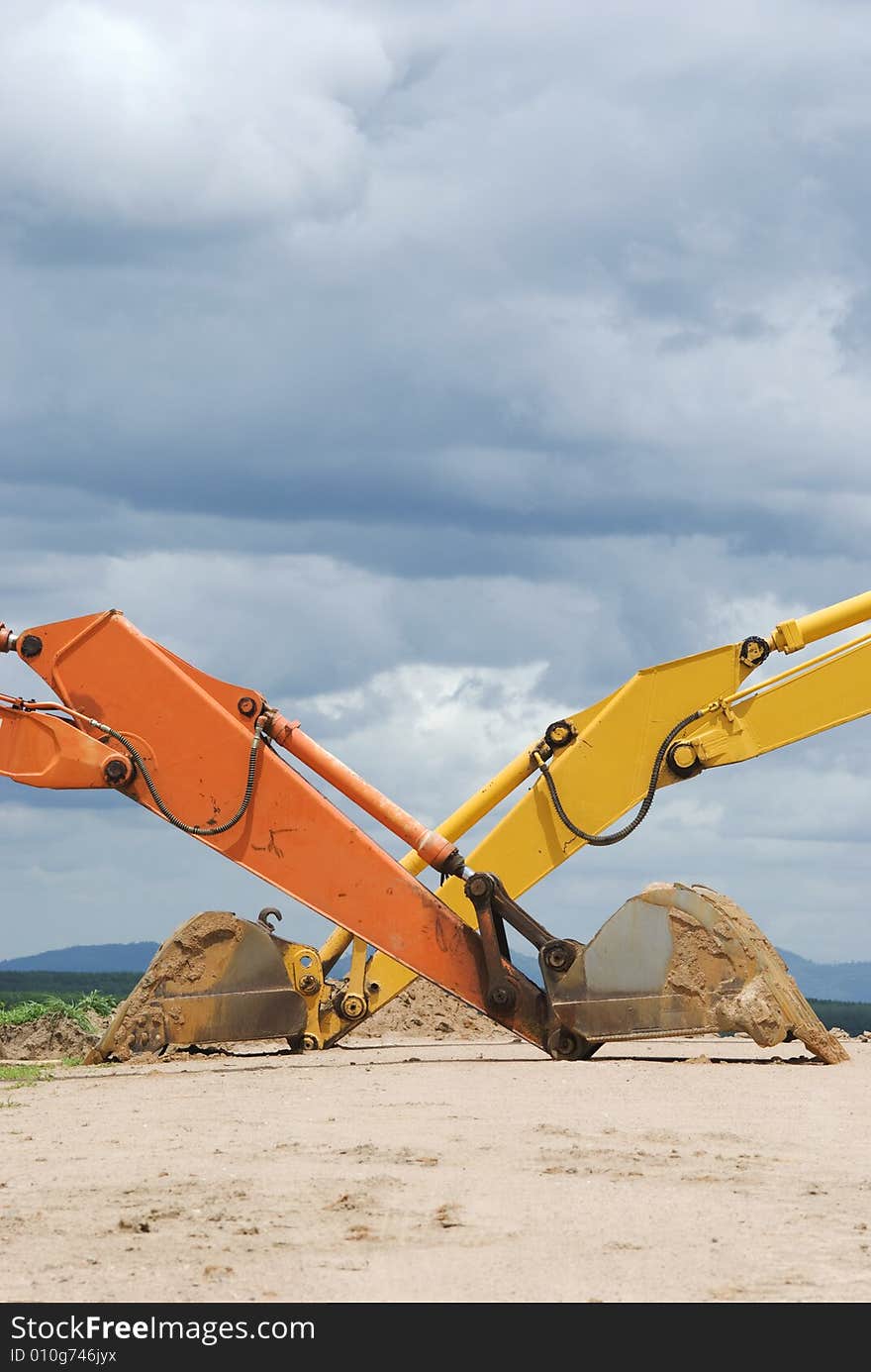 Scoops of two excavators crossing, with landscape and a cloudy sky in the background. Scoops of two excavators crossing, with landscape and a cloudy sky in the background