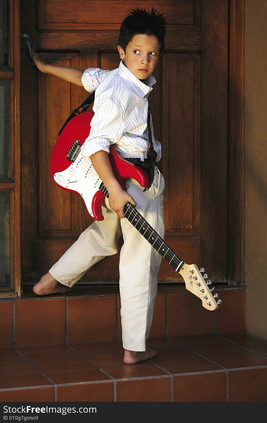 Boy standing up opening door with red guitar. Boy standing up opening door with red guitar