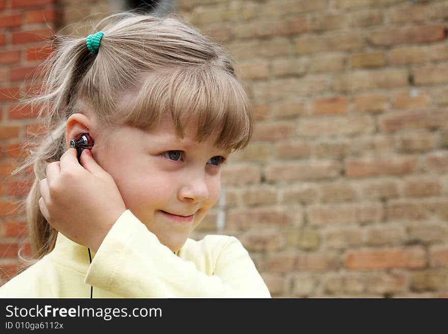 The girl listens to music on a background of a brick wall