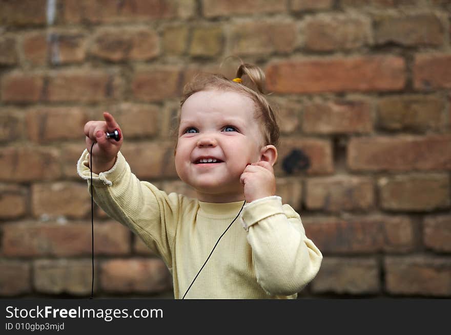 The baby listens to music on a background of a brick wall. The baby listens to music on a background of a brick wall