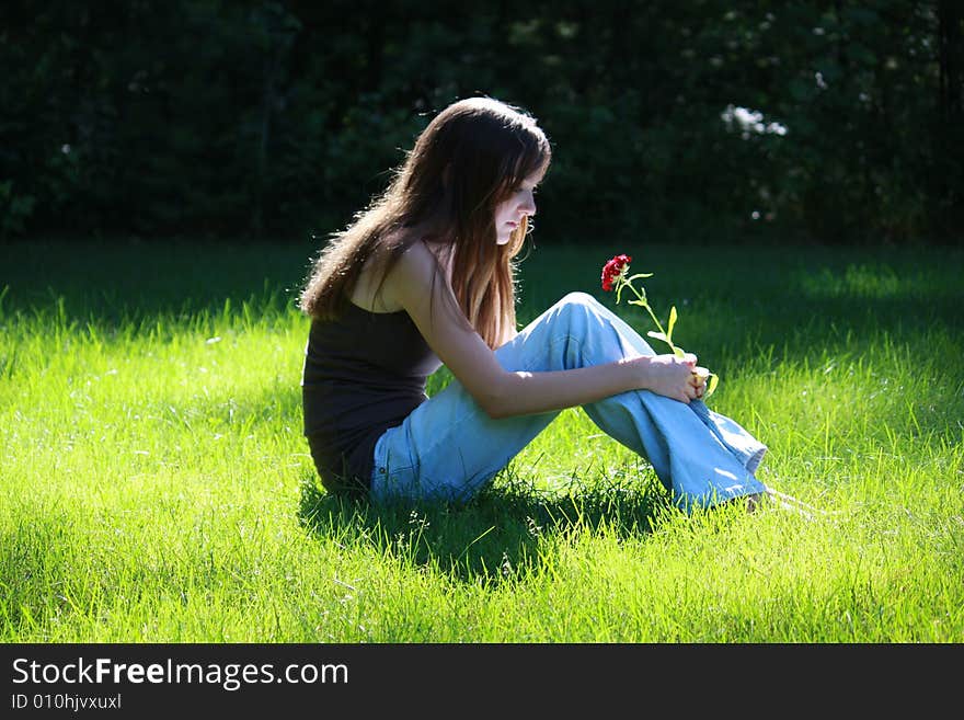 Female teenager sitting in the grass looking thoughtfully at a flower. Female teenager sitting in the grass looking thoughtfully at a flower.